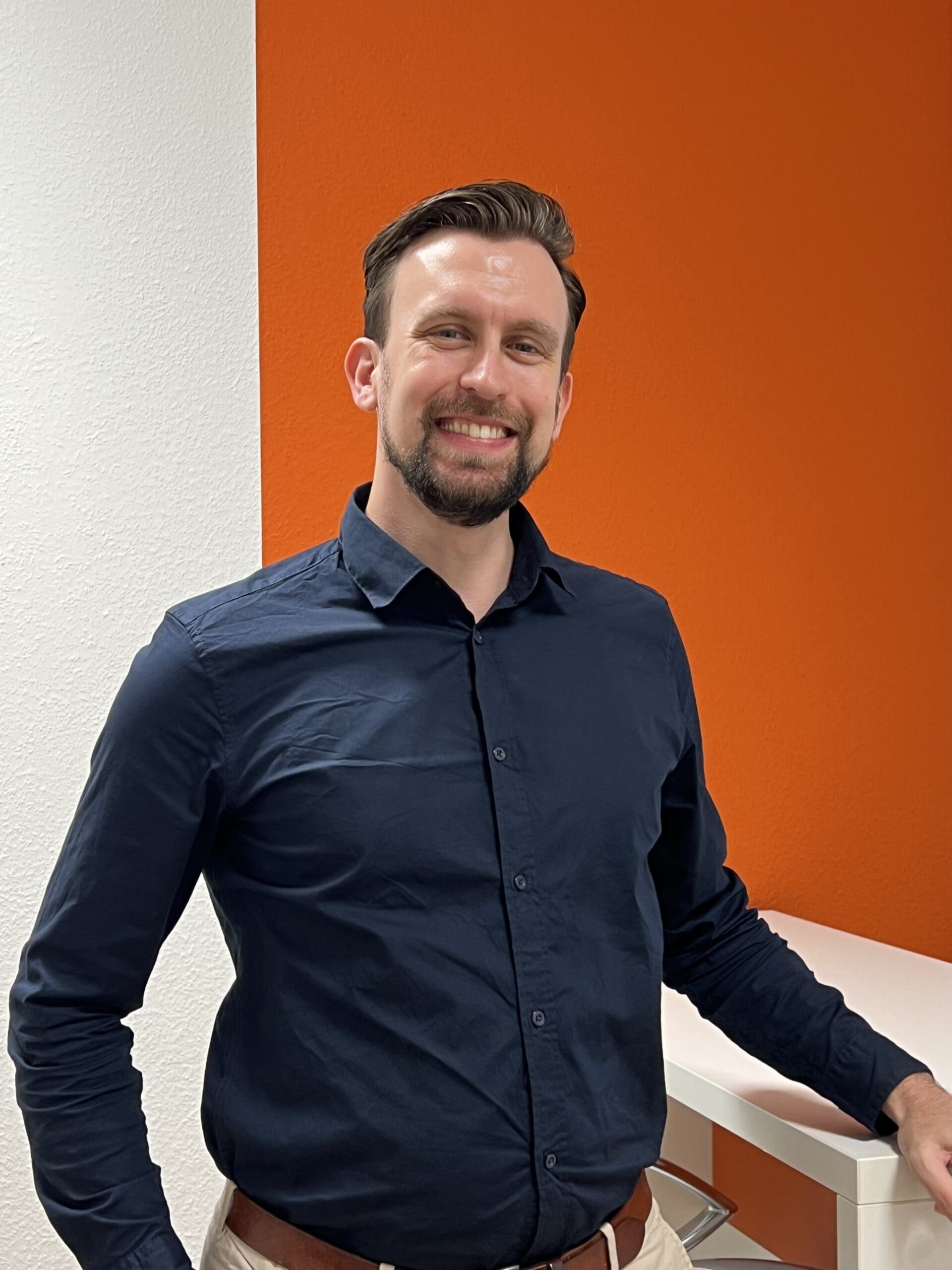 Lächelnder Mann im schwarzen Hemd vor orangefarbener Wand